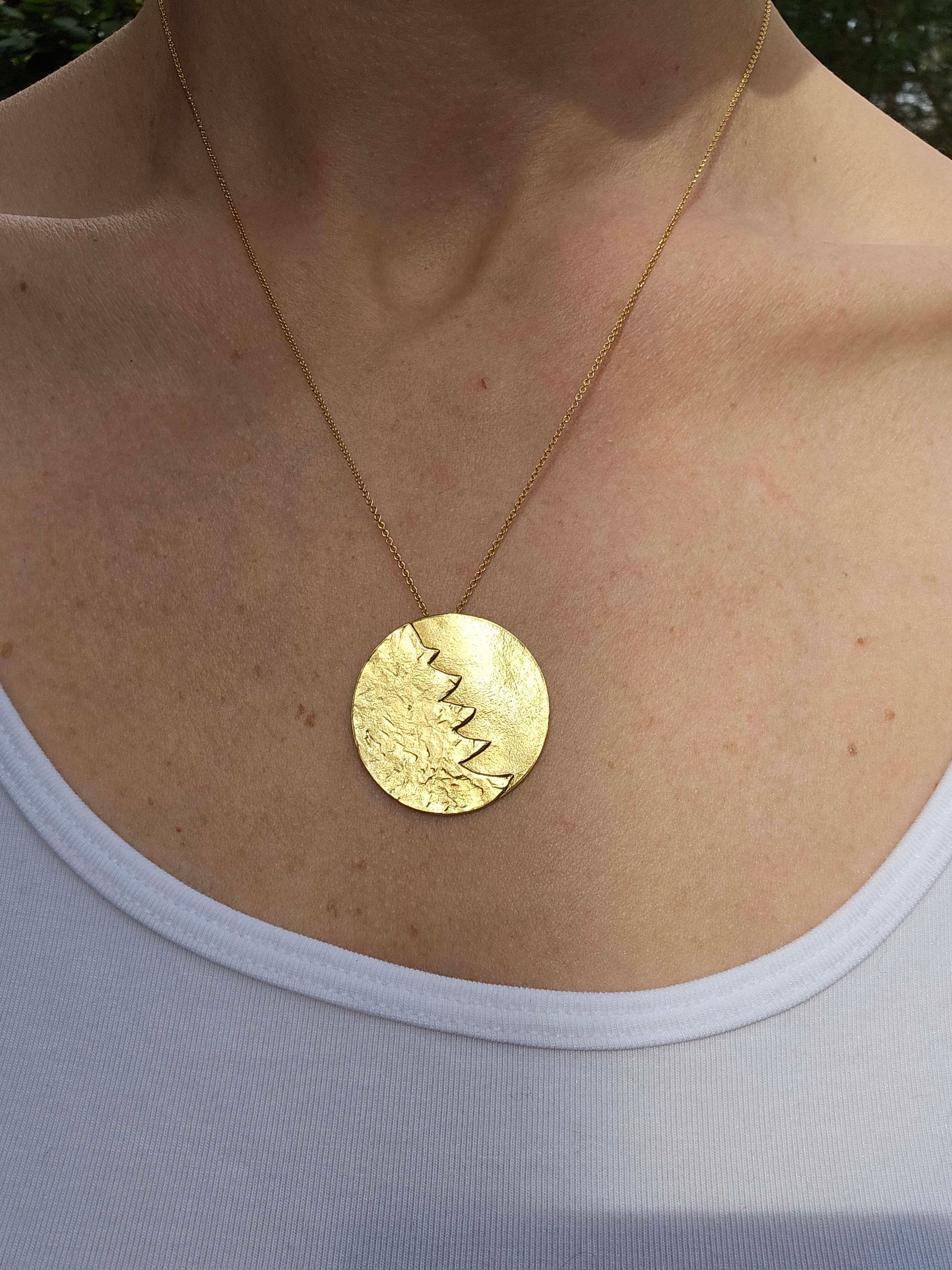 A woman wearing a gold pendant and white shirt.