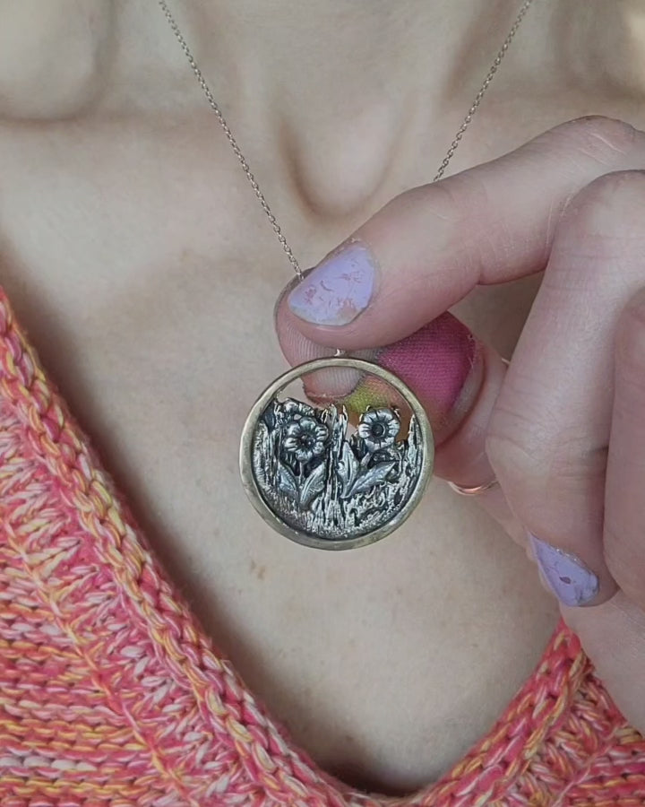 one-of-a-kind jewelry necklace held between woman's fingers with an orange sweater